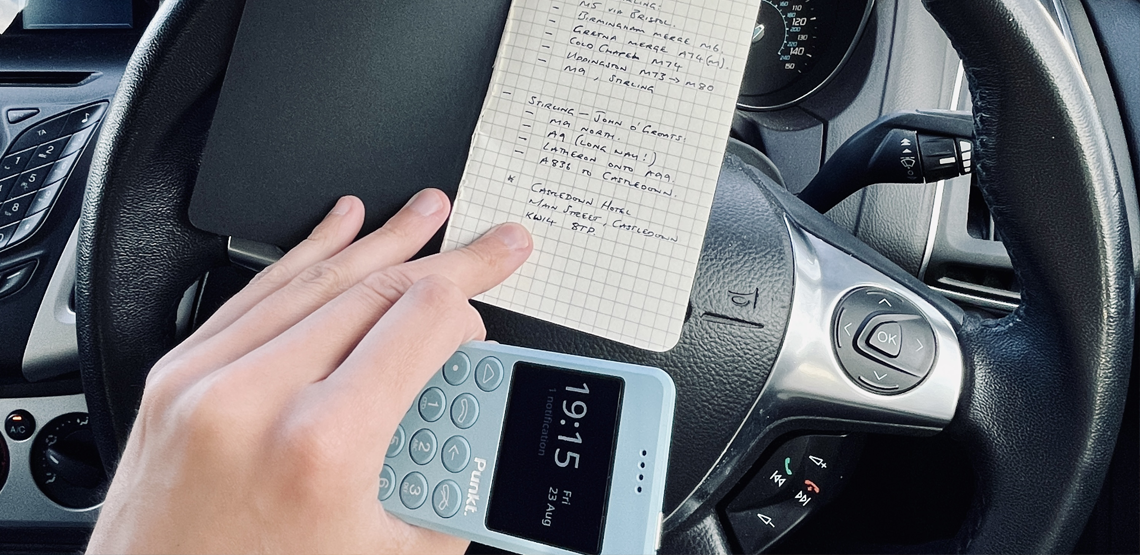 Punkt. MP02 in hand in a car on a road trip and a blocknote