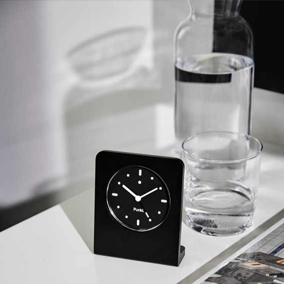 Punkt. AC02 alarm clock next to a glass carafe with water on a white table