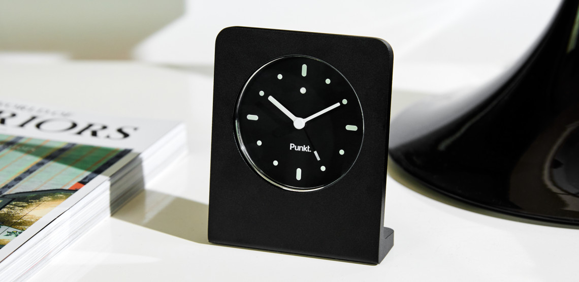 Punkt ac02 alarm clock black on a desk next to a magazine